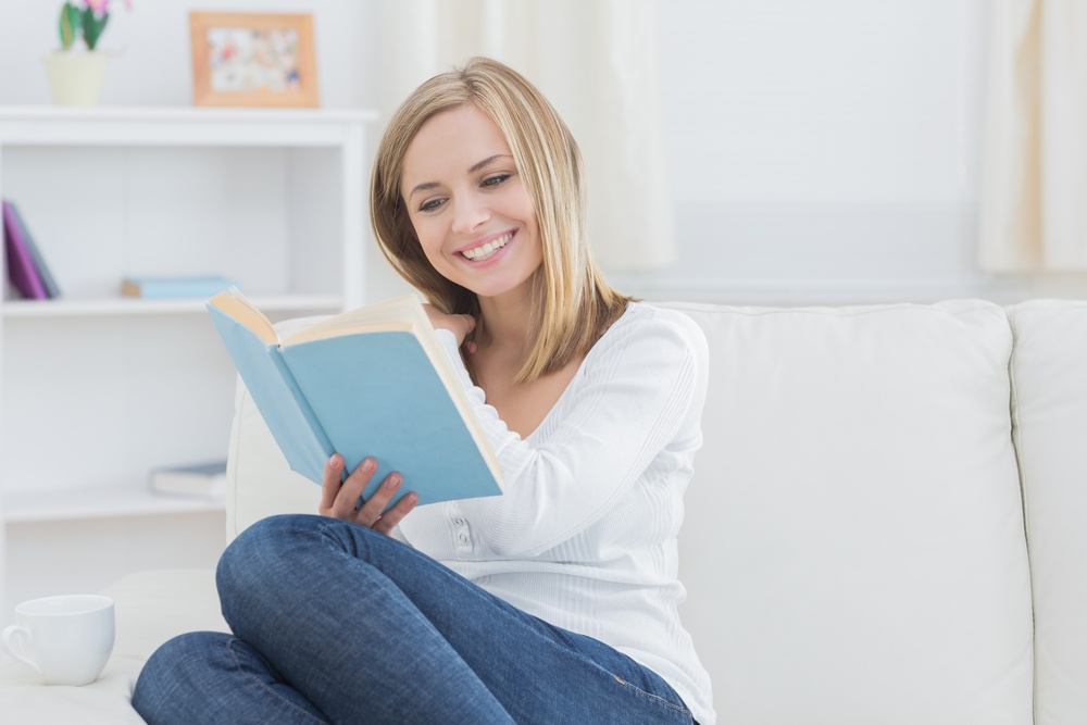 Happy young woman reading storybook on couch at home